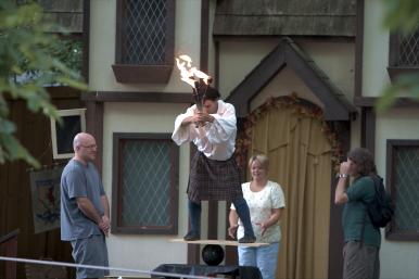 Typical guy in kilt balancing on bowling ball using a rickety table while preparing to juggle flaming torches.