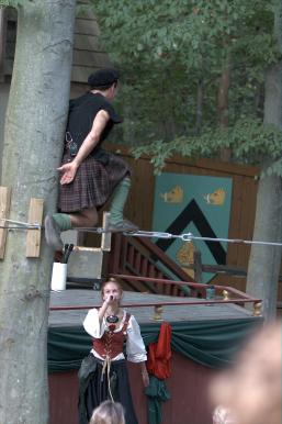 Man in kilt on tight rope above crowd proposes on one knee.
